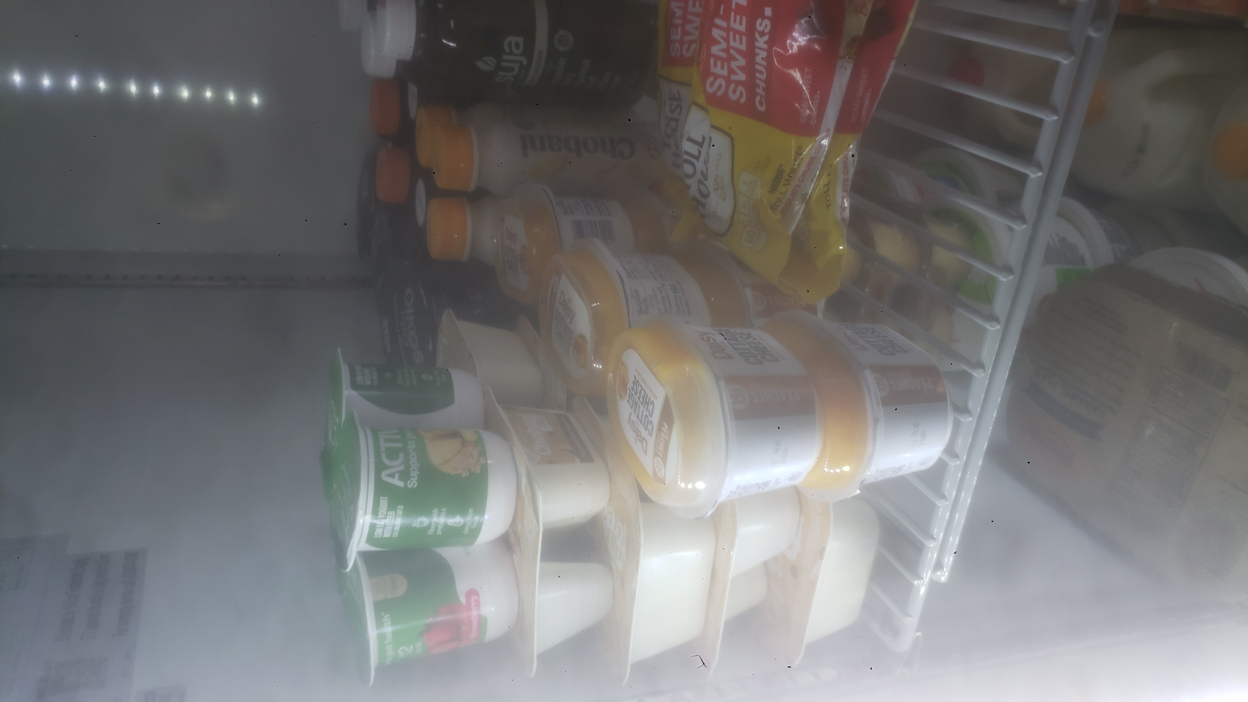 Bags of semi-sweet chocolate chucks, cups of yogurt, small containers of cottage cheese, and bottles of juice in a fridge.